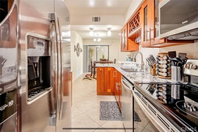 353 N Hermosa Dr Unit 7C1, Palm Springs, CA 92262 - kitchen with appliances with stainless steel finishes, brown cabinets, a sink, light tile patterned floors, and light stone counters