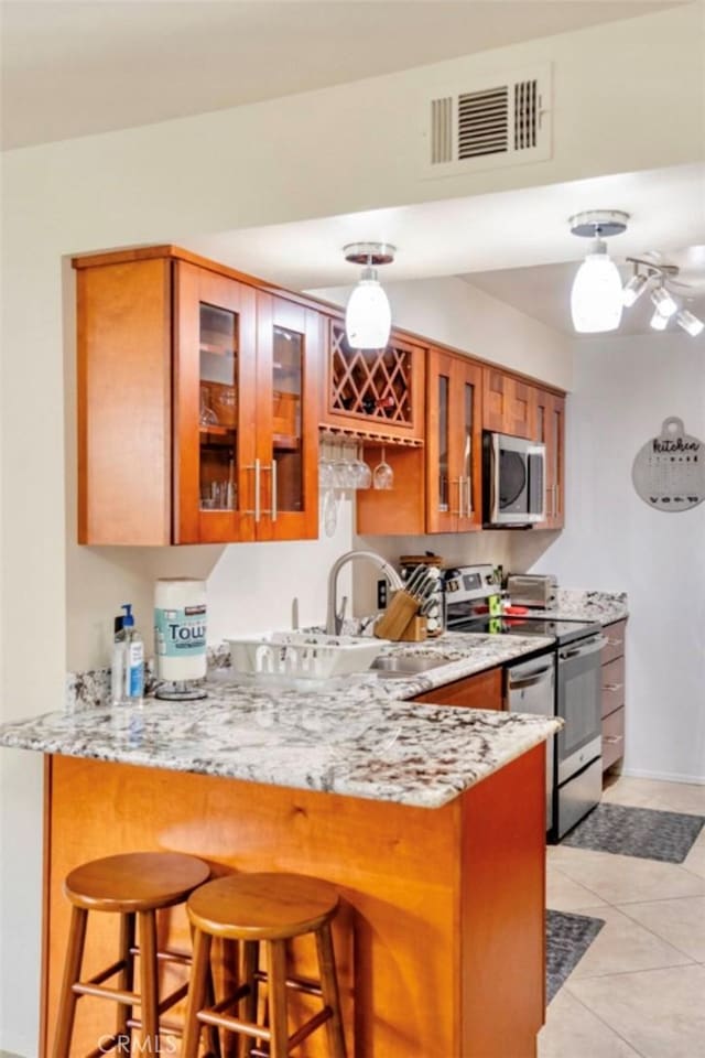 353 N Hermosa Dr Unit 7C1, Palm Springs, CA 92262 - kitchen featuring stainless steel appliances, brown cabinetry, a peninsula, and a breakfast bar