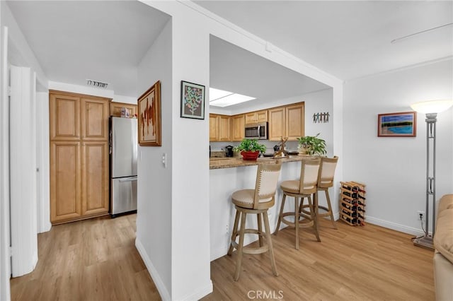 4240 Lost Hills Rd Unit 2102, Calabasas, CA 91301 - kitchen featuring appliances with stainless steel finishes, light wood finished floors, baseboards, a breakfast bar area, and brown cabinetry