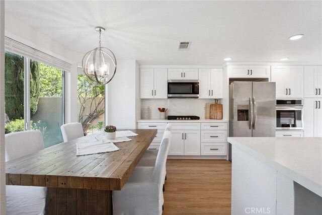 24775 Calle Serranona, Calabasas, CA 91302 - kitchen with stainless steel appliances, a chandelier, white cabinets, pendant lighting, and light wood finished floors