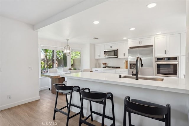 24775 Calle Serranona, Calabasas, CA 91302 - kitchen with appliances with stainless steel finishes, a sink, light countertops, white cabinetry, and a kitchen breakfast bar