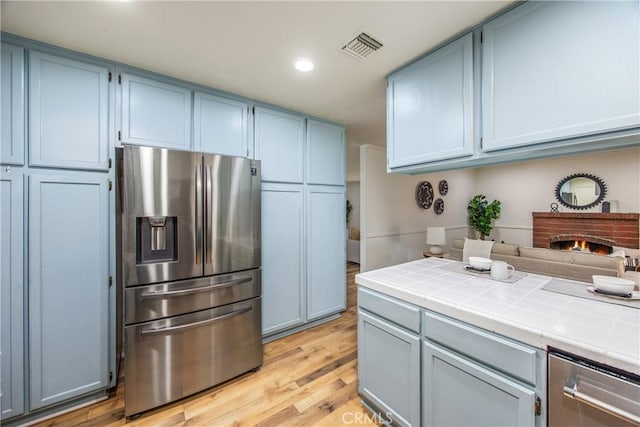 1456 Fernwood Dr, Redlands, CA 92374 - kitchen with stainless steel fridge, tile counters, light wood finished floors, recessed lighting, and blue cabinetry