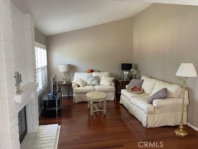 23192 Villena, Mission Viejo, CA 92692 - living area featuring wood finished floors, a brick fireplace, vaulted ceiling, and baseboards