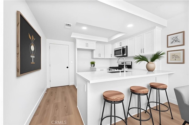 659 Valley Oak Ln, Newbury Park, CA 91320 - kitchen featuring stainless steel microwave, a peninsula, white cabinetry, a breakfast bar, and baseboards