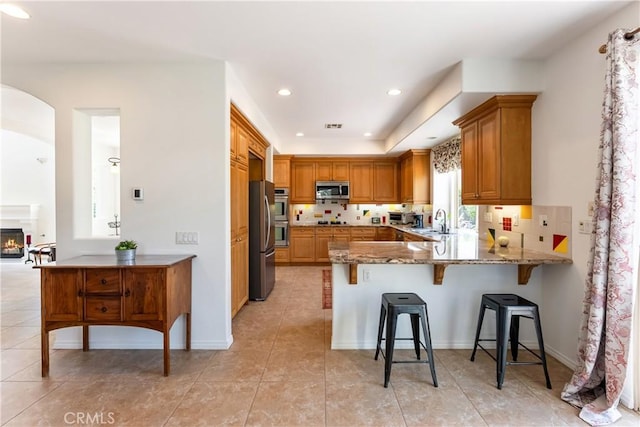 7659 Balasiano Ave, West Hills, CA 91304 - kitchen featuring appliances with stainless steel finishes, a peninsula, a sink, a breakfast bar, and stone countertops