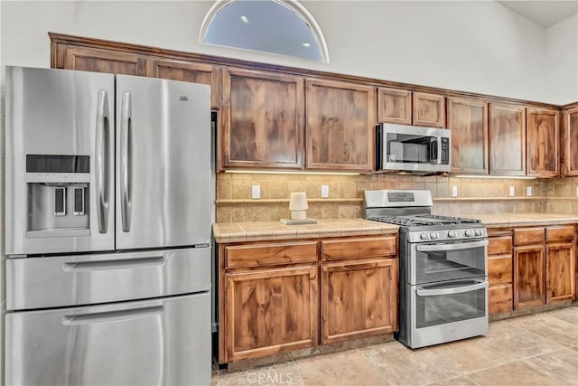 300 S Lombardi St, Porterville, CA 93257 - kitchen with stainless steel appliances, tile countertops, tasteful backsplash, and brown cabinetry