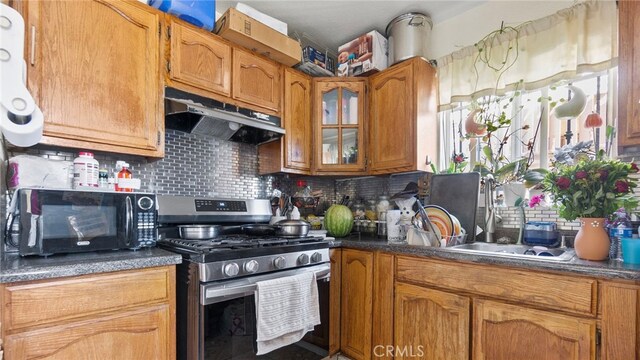 413 E 81st St, Los Angeles, CA 90003 - kitchen featuring stainless steel gas stove, black microwave, under cabinet range hood, tasteful backsplash, and dark countertops