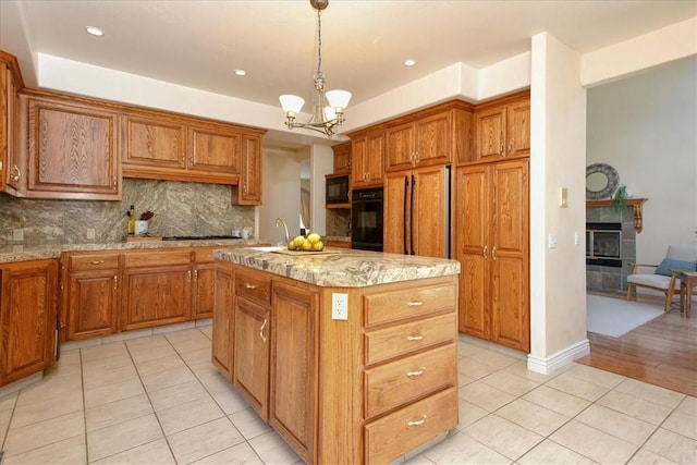 455 Chiswick Way, Cambria, CA 93428 - kitchen with light tile patterned flooring, black appliances, an island with sink, decorative backsplash, and a tiled fireplace