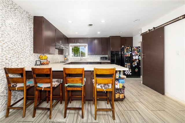 22892 Palm Ave, Grand Terrace, CA 92313 - kitchen featuring black appliances, a peninsula, under cabinet range hood, a barn door, and light countertops