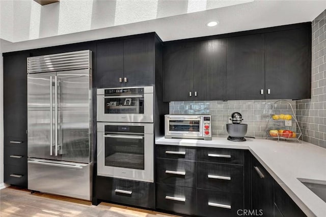 1821 Overview Cir, North Tustin, CA 92705 - kitchen with appliances with stainless steel finishes, dark cabinetry, light wood finished floors, light countertops, and backsplash