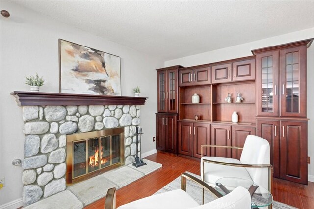 10139 Sun Valley Dr, Rancho Cucamonga, CA 91737 - living area featuring wood finished floors, a stone fireplace, a textured ceiling, and baseboards