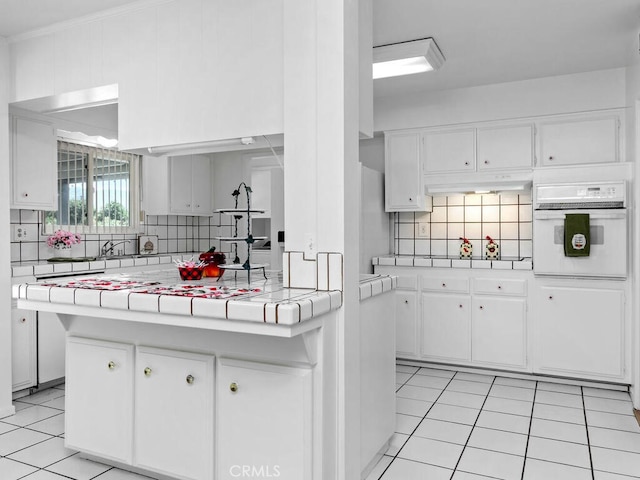 29412 Carmel Rd, Menifee, CA 92586 - kitchen featuring oven, a peninsula, tile countertops, decorative backsplash, and white cabinetry