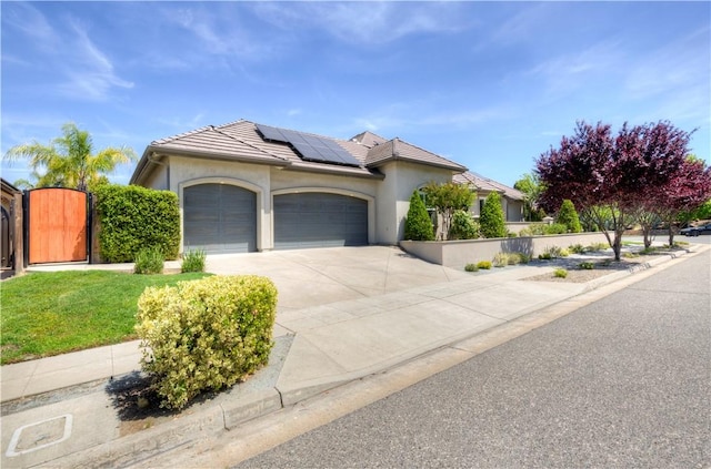 2096 E Olympic Ave, Fresno, CA 93730 - ranch-style house with an attached garage, roof mounted solar panels, stucco siding, and a gate