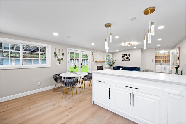 13824 Powers Rd, Poway, CA 92064 - kitchen featuring light wood finished floors, a large fireplace, white cabinets, light countertops, and decorative light fixtures