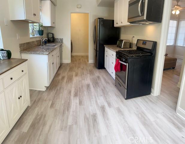 11529 De Celis Pl, Granada Hills, CA 91344 - kitchen with appliances with stainless steel finishes, light wood-style floors, white cabinetry, and baseboards