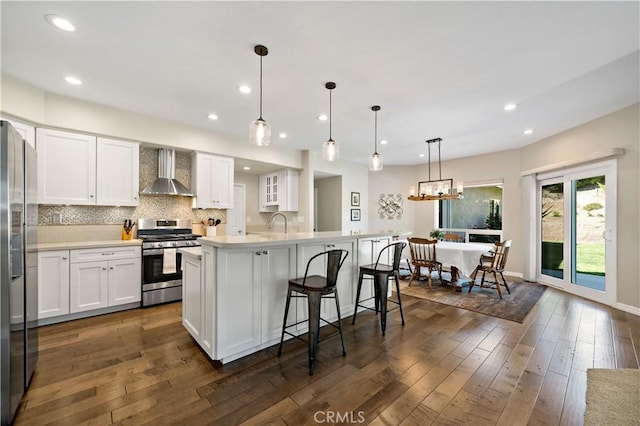 31484 Britton Cir, Temecula, CA 92591 - kitchen with wall chimney range hood, appliances with stainless steel finishes, a breakfast bar area, white cabinets, and dark wood-style floors