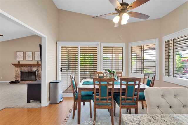 13950 High Falls Trl, Apple Valley, CA 92307 - dining room featuring ceiling fan, light wood-style floors, a fireplace, baseboards, and vaulted ceiling