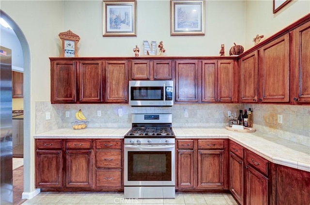 2267 Lorena Ave, Sanger, CA 93657 - kitchen featuring appliances with stainless steel finishes, arched walkways, tasteful backsplash, tile countertops, and light tile patterned floors