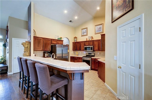 2267 Lorena Ave, Sanger, CA 93657 - kitchen featuring appliances with stainless steel finishes, a peninsula, a breakfast bar area, high vaulted ceiling, and tasteful backsplash