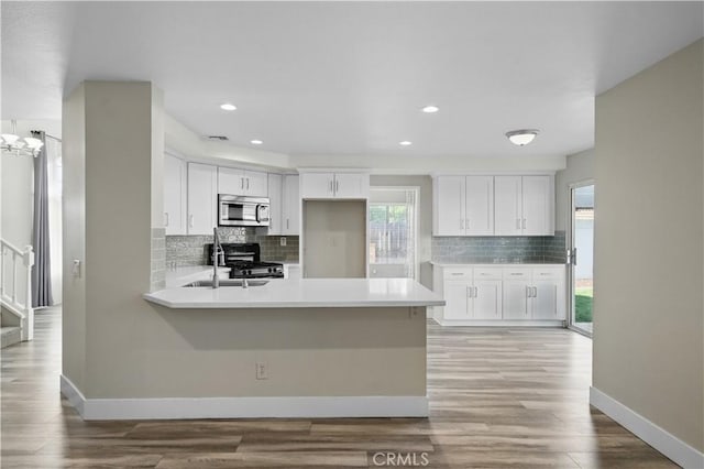 31070 Larchwood St, Menifee, CA 92584 - kitchen with stainless steel microwave, white cabinets, black range with gas stovetop, a peninsula, and backsplash