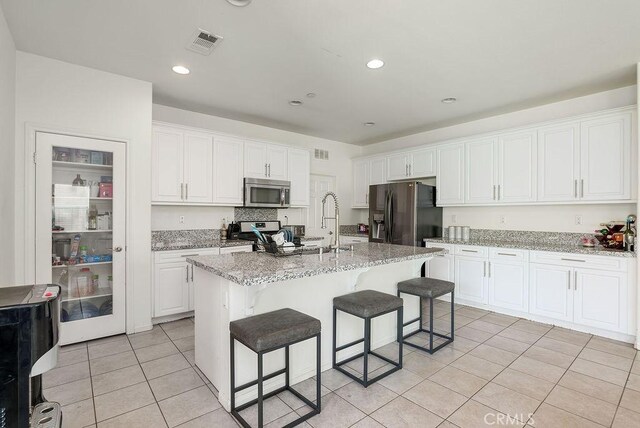 706 Leather Oak Ln, Pomona, CA 91766 - kitchen featuring stainless steel appliances, light tile patterned floors, white cabinets, a breakfast bar area, and light stone countertops