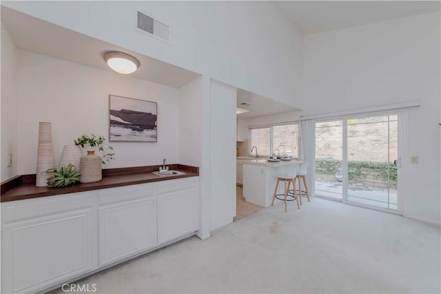 2501 Tiffany Pl, Fullerton, CA 92833 - kitchen featuring a sink, light carpet, white cabinetry, healthy amount of natural light, and a towering ceiling