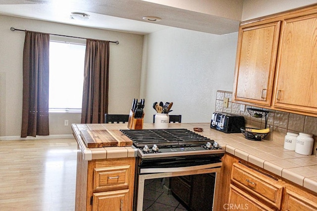 915 Moran Ct, Paso Robles, CA 93446 - kitchen featuring stainless steel range with gas stovetop, decorative backsplash, tile countertops, a peninsula, and baseboards