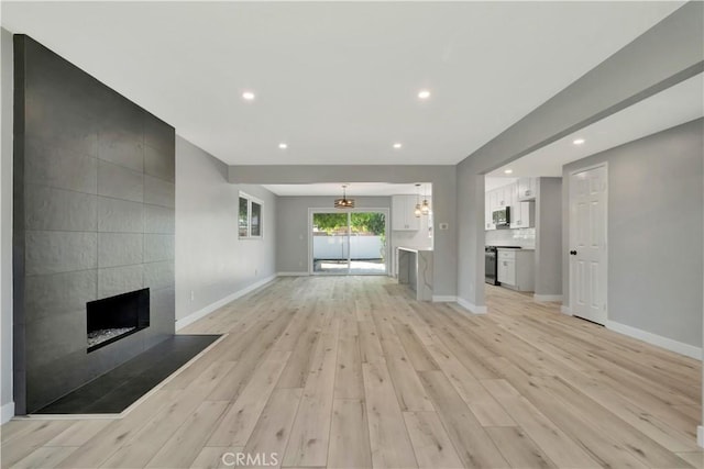 7741 Shoup Ave, West Hills, CA 91304 - unfurnished living room with a tiled fireplace, baseboards, recessed lighting, light wood-style floors, and a chandelier