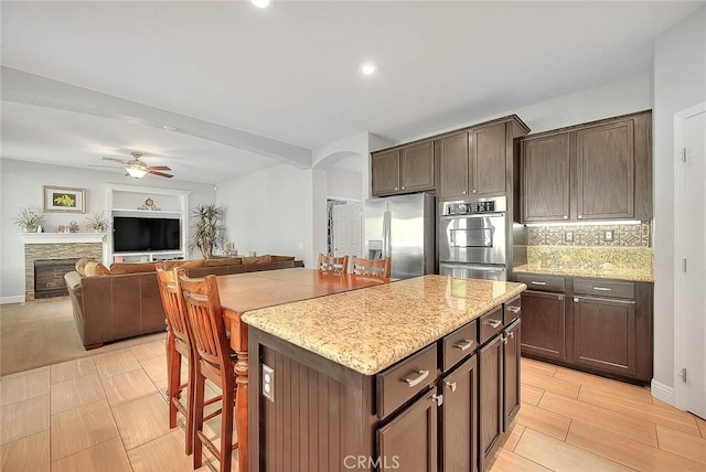 8758 Aspen Ct, Riverside, CA 92508 - kitchen with stainless steel appliances, arched walkways, a kitchen island, light stone counters, and ceiling fan