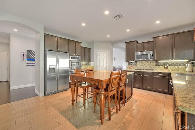 8758 Aspen Ct, Riverside, CA 92508 - kitchen featuring stainless steel appliances, arched walkways, dark brown cabinets, decorative backsplash, and a sink