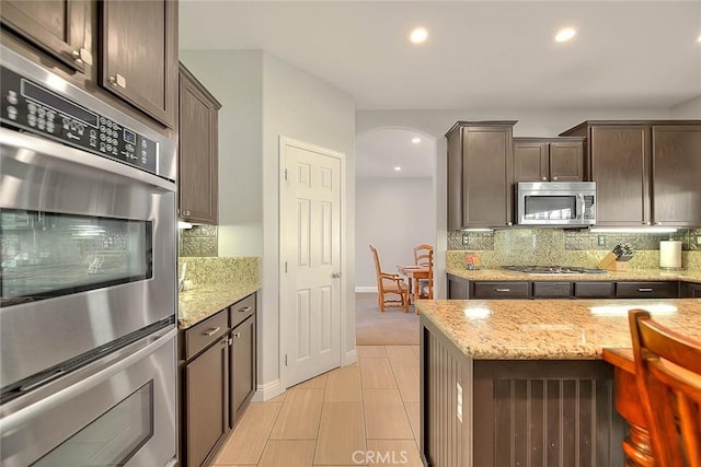 8758 Aspen Ct, Riverside, CA 92508 - kitchen featuring appliances with stainless steel finishes, backsplash, dark brown cabinets, recessed lighting, and light stone counters