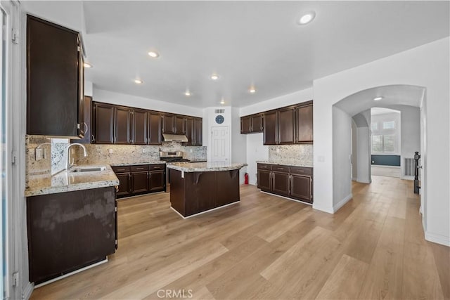 8840 Greenlawn St, Riverside, CA 92508 - kitchen with under cabinet range hood, arched walkways, dark brown cabinetry, a kitchen island, and a sink