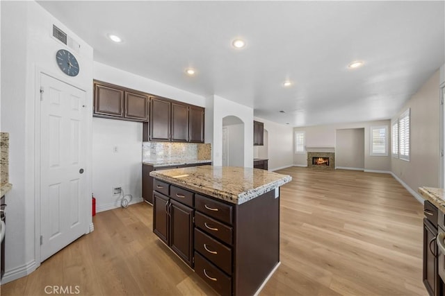 8840 Greenlawn St, Riverside, CA 92508 - kitchen with light wood-style flooring, dark brown cabinetry, a warm lit fireplace, light stone counters, and recessed lighting