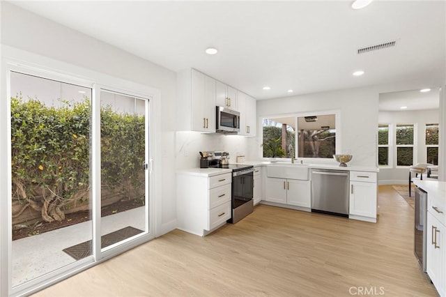 7848 Calmcrest Dr, Downey, CA 90240 - kitchen featuring appliances with stainless steel finishes, a sink, light wood finished floors, white cabinets, and recessed lighting