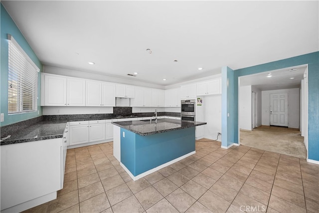 11877 Crossbill Way, Jurupa Valley, CA 91752 - kitchen with white cabinetry, light tile patterned flooring, dark stone countertops, double oven, and a center island with sink