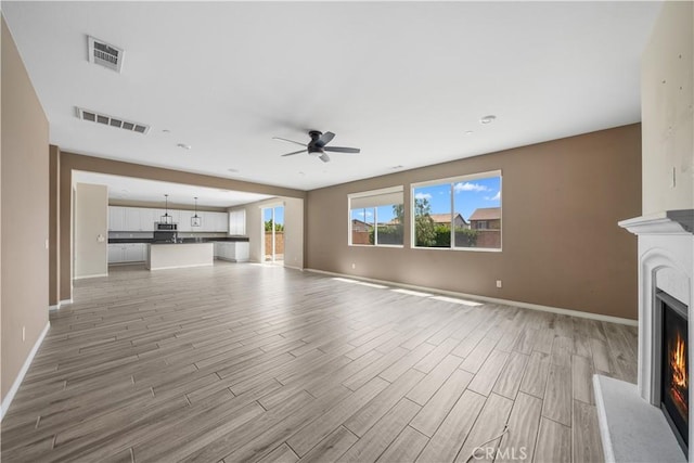 11836 Crossbill Way, Jurupa Valley, CA 91752 - unfurnished living room featuring a warm lit fireplace, baseboards, light wood finished floors, and a ceiling fan