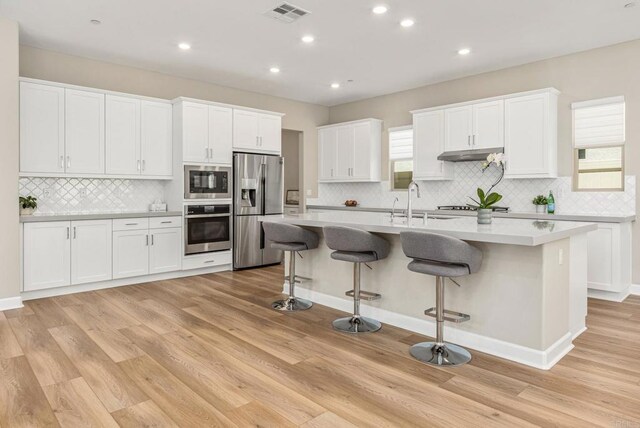675 Westbrook Loop, San Marcos, CA 92078 - kitchen with stainless steel appliances, tasteful backsplash, a kitchen island with sink, light wood-style floors, and white cabinetry