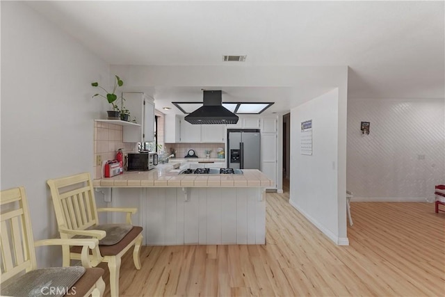 7558 Lobos Ave, Hesperia, CA 92345 - kitchen featuring appliances with stainless steel finishes, tile counters, a peninsula, light wood-type flooring, and white cabinets