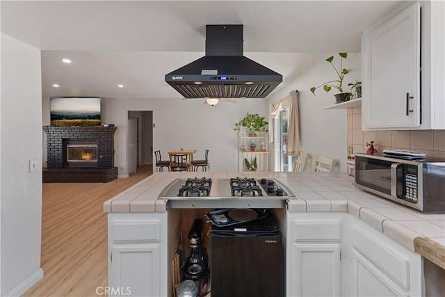 7558 Lobos Ave, Hesperia, CA 92345 - kitchen with extractor fan, stainless steel appliances, a peninsula, tile countertops, and a brick fireplace