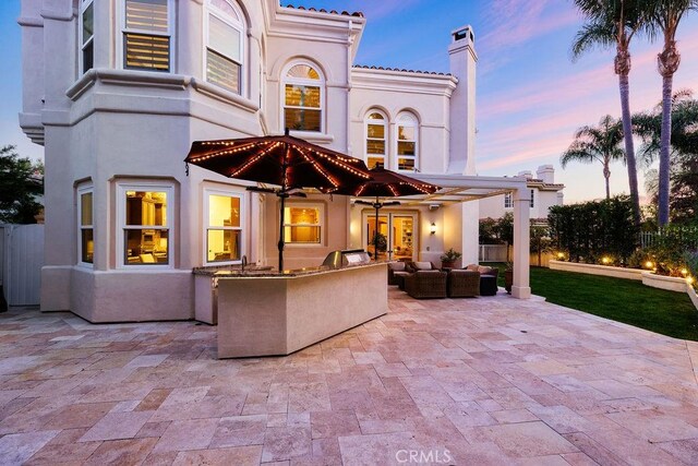 30801 Via Conquista, San Juan Capistrano, CA 92675 - back of house at dusk with a patio area, exterior kitchen, a chimney, and stucco siding