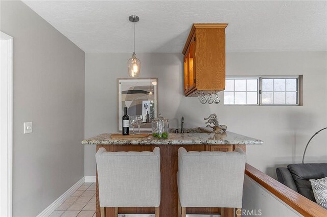 435 Orlena Ave, Long Beach, CA 90814 - kitchen with light tile patterned floors, brown cabinets, baseboards, light stone counters, and pendant lighting