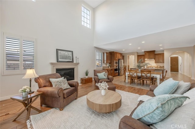 24923 Hearth Ct, Valencia, CA 91354 - living area with arched walkways, light wood-type flooring, a glass covered fireplace, a towering ceiling, and baseboards