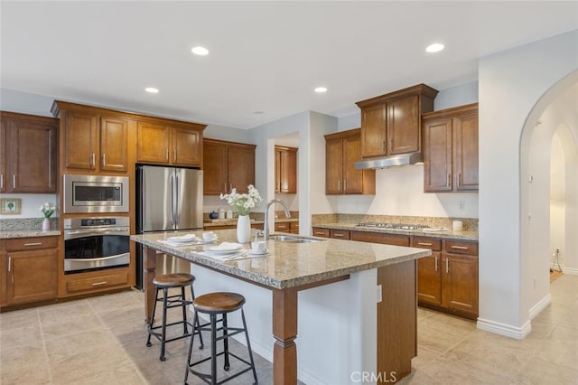 24923 Hearth Ct, Valencia, CA 91354 - kitchen featuring appliances with stainless steel finishes, a sink, under cabinet range hood, arched walkways, and a kitchen breakfast bar