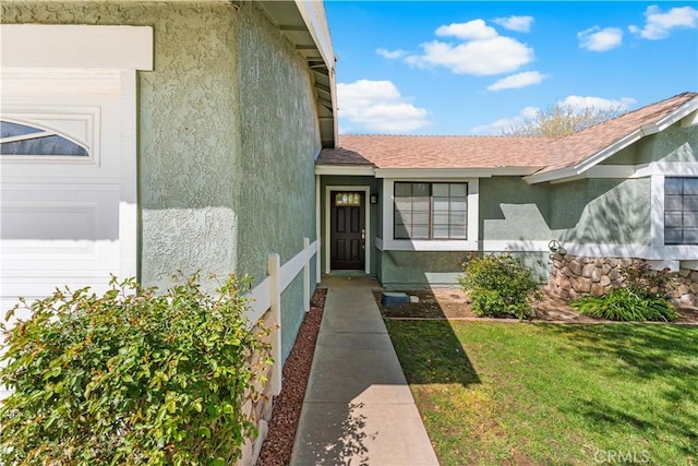38115 41st St E, Palmdale, CA 93552 - doorway to property featuring stucco siding, a shingled roof, and a lawn