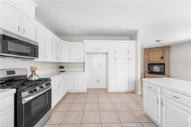 43453 Tali St, Lancaster, CA 93535 - kitchen featuring appliances with stainless steel finishes, tile counters, white cabinetry, light tile patterned flooring, and a fireplace