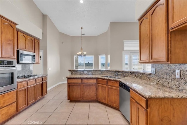 17322 Danbury Ave, Hesperia, CA 92345 - kitchen featuring appliances with stainless steel finishes, a chandelier, backsplash, brown cabinetry, and light stone countertops