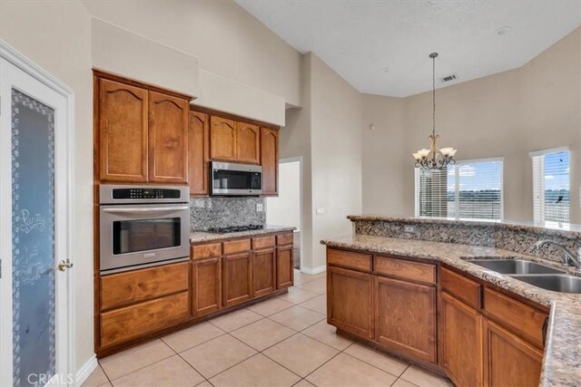 17322 Danbury Ave, Hesperia, CA 92345 - kitchen featuring appliances with stainless steel finishes, a towering ceiling, brown cabinetry, a chandelier, and decorative backsplash