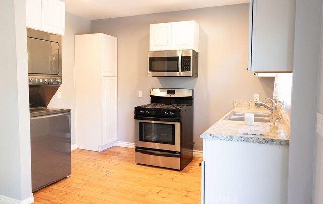14816 Covello St, Van Nuys, CA 91405 - kitchen with appliances with stainless steel finishes, stacked washer / drying machine, a sink, light wood-style floors, and white cabinets