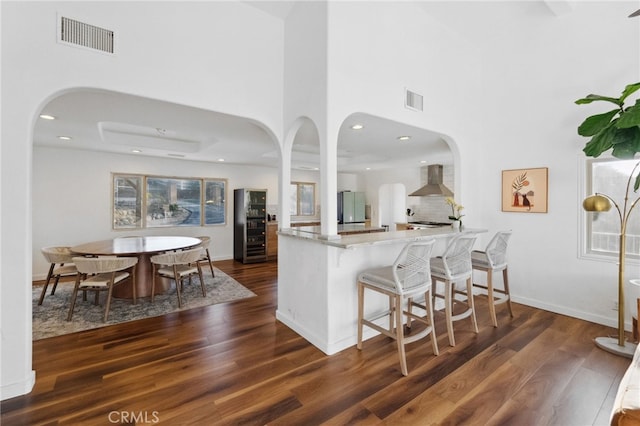 44310 Calle Bernardo, Temecula, CA 92590 - kitchen featuring wall chimney range hood, wood finished floors, a high ceiling, arched walkways, and a peninsula