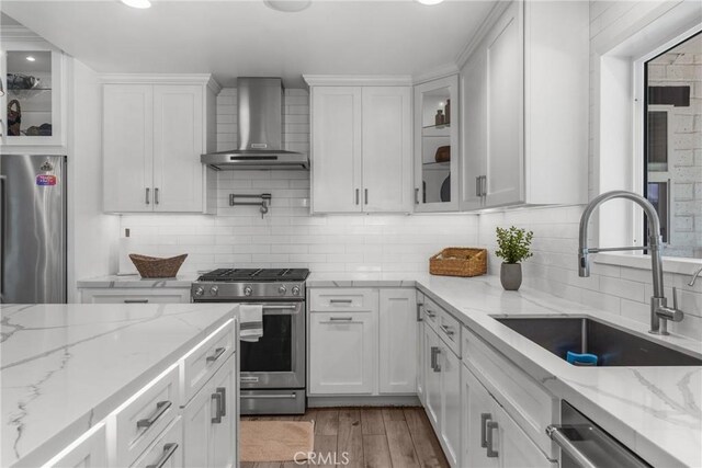 4674 Norton Pl, Riverside, CA 92506 - kitchen featuring appliances with stainless steel finishes, wall chimney range hood, a sink, white cabinets, and decorative backsplash